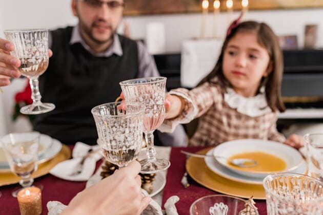 Crop father and daughter clinking glasses of alcoholic drink against unrecognizable mother at table during New Year holiday at home, Model released, Property released SiAndSi_Christmas_95.jpg Copyright: xSixAndxSix MR