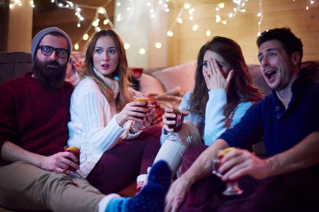 IMAGO Creative, Weihnachten, Tradition: Weihnachtsfilme sehen Friends enjoying mulled wine in chalet, 10.02.2017, Copyright: xGpointstudiox, model released, drinking,holding,celebrating,watching television,differential focus,three quarter length,at home,surprise,bonding,festive,fun,togetherness,friendship,happiness,relaxation,christmas light,young adult,20 to 24 years,25 to 29 years,female,woman,young woman,male,man,young man,heterosexual couple,young couple,four people,cabin,indoors,winter,knit hat,sock,christmas,laughing,mouth open,smiling,leisure,movie,enjoyment,both male and female,mulled wine,covering eyes,christmas party,legs outstretched,February 2017 Release,Consuming Food,Drinking,Holding,Watching,Watching TV,Young Adult,20-24 Years,25-29 Years,Female,Women,Young Women,Young Adult Woman,Ma Ref:IS09B509R