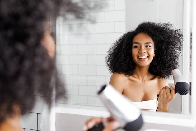 A young woman blow drying her hair in front of a mirror Copyright: xxArtemxVarnitsinx