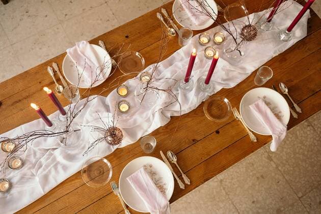 From above of white tablecloth and plates placed on festive table decorated with burning candles and dry branches of tree, Property released GustavoPozo_ChristmasDecoration_68.jpg Copyright: xGustavoxPozox Model Released