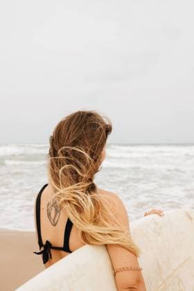 Back view of unrecognizable young sportswoman in swimwear with surfboard looking away on sandy coast against stormy ocean, Model released, Property released LeoPastor_YoungWomanSurf_2.jpg Copyright: xLeoxPastorx MR