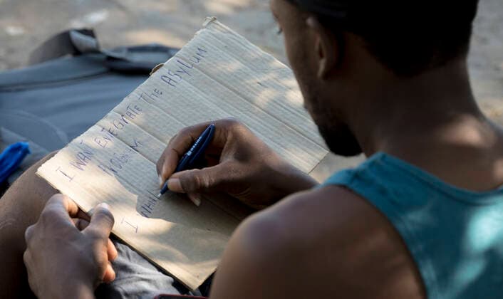(210925) -- CIUDAD ACUNA (MEXICO), Sept. 25, 2021 -- A Haitian migrant writes a sign seeking asylum before crossing into the United States, in Ciudad Acuna, Mexico, on Sept. 25, 2021. U.S.-Mexico border arrests have reportedly stayed at the highest level in more than two decades, with more than 208,000 registered in August alone. (Photo by Xinhua) MEXICO-CIUDAD ACUNA-U.S.-BORDER-MIGRANTS NickxWagner 