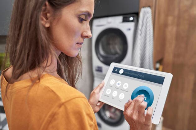 Woman using digital tablet to operate washing machine at home model released Symbolfoto property released ABIF01487
