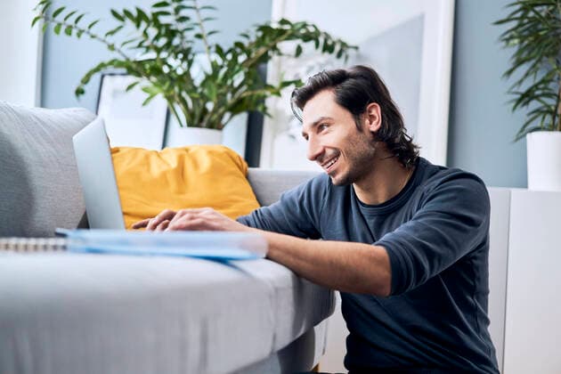 Smiling male student using laptop while learning at home model released Symbolfoto property released BSZF01854