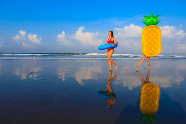 IMAGO Creative: Frühlingsferien und reisen Female friends holding swimming floats while walking at beach model released Symbolfoto EAF00116