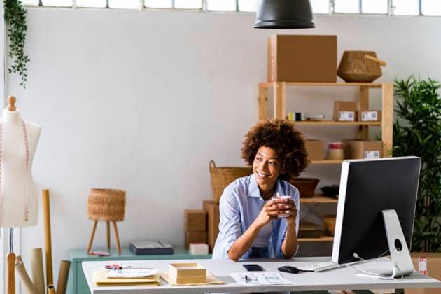 Smiling female design professional holding mug while sitting at desk in studio model released Symbolfoto property released GIOF13479