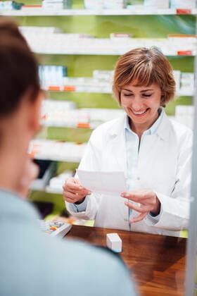 Smiling pharmacist reading prescription while standing with customer in store model released Symbolfoto property released JOSEF05414