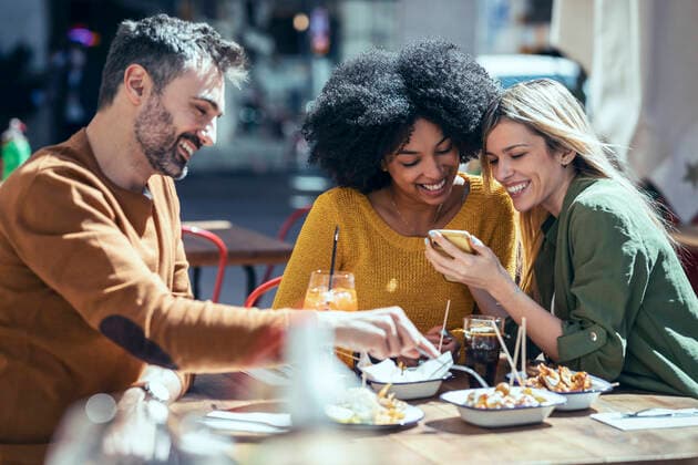 IMAGO Creative, Food, Tapas Happy female friends sharing mobile phone by male friend at restaurant model released Symbolfoto property released JSRF01606