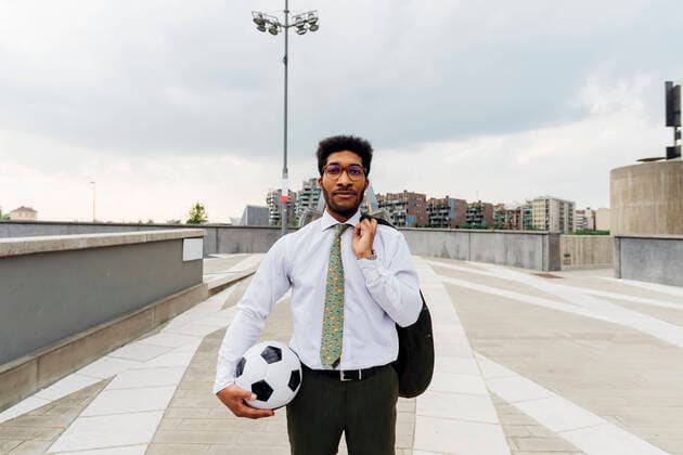 IMAGO Creative: Sport in der Stadt Businessman holding sports ball and blazer while standing on footpath model released Symbolfoto MEUF04146