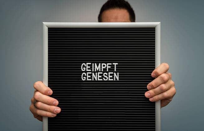 Mann hält Schild in der Hand mit der Aufschrift Geimpft und Genesen Covid-19 Coronavirus 2G-Regel, 2G schließt ungeimpfte Menschen aus, Getestet Geimpft und Genesen in Deutschland