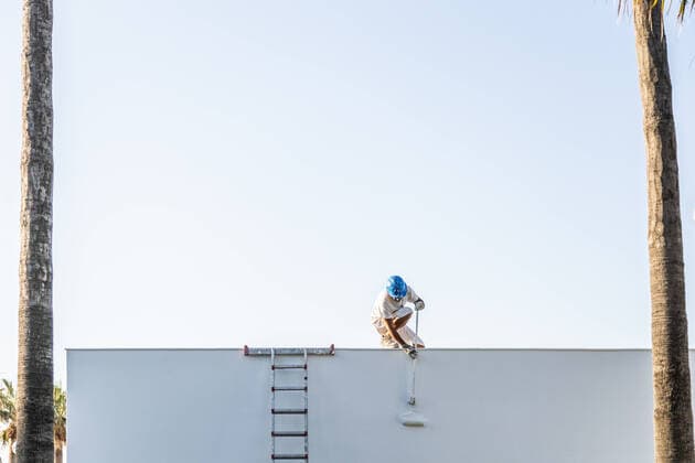 Unrecognizable young painter painting the facade of an apartment with a roller from the roof and the staircase on the side DavidFuentes_Painter_9.jpg Copyright: xDavidxFuentesx Model Released