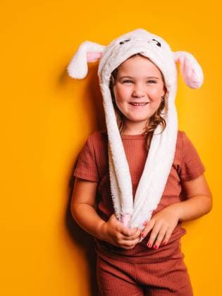 Happy cute little girl with brown hair and nails manicured in casual clothes and white hat with bunny ears standing and looking away against yellow background in studio, Model released HodeiUnzueta_KidsYellowBackground_2.jpg Copyright: xHodeixUnzuetax MR