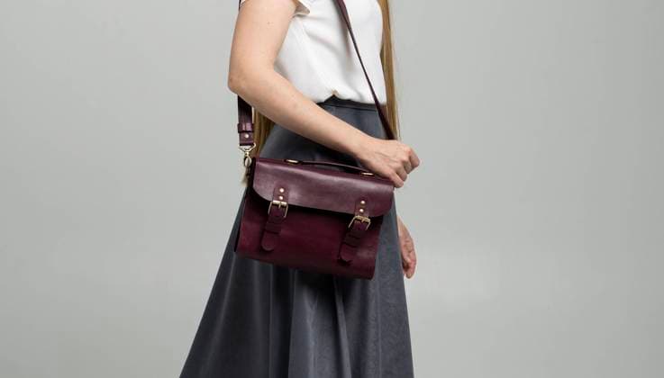 Small red leather bag over a woman shoulder on a white background. Shoulder handbag. Woman in a white shirt and grey skirt and with a red handbag. Style, retro, fashion, vintage and elegance. Small red leather bag over a woman shoulder on a white background. Shoulder handbag. Woman in a white shirt and grey skirt and with a ted handbag. Style, retro, fashion, vintage and elegance Copyright: xx 35395706