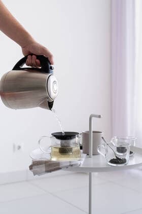 IMAGO Creative: Haushaltsgeräte - Wasserkocher Close up of coffee table and man hand holding kettle, pouring hot water for making tea Making tea. Close up of coffee table and man hand holding kettle, pouring hot water for making tea Copyright: xx 38526858