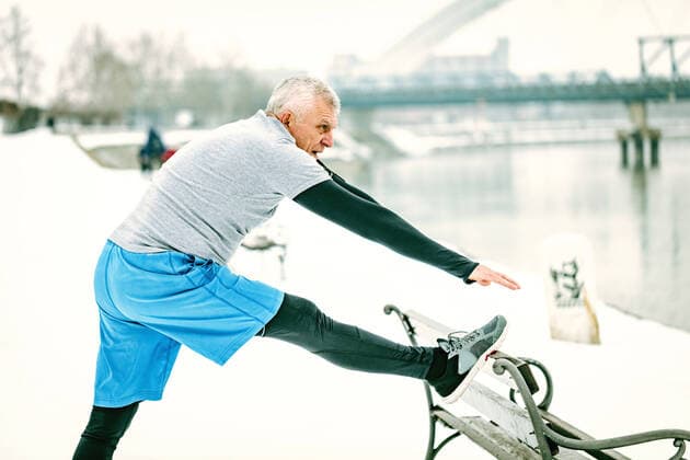 IMAGO Creative: Alternativer Wintersport Stretching By The River Active senior man athlete stretching leg on the bench and doing exercises by the river during the winter training outside in. Copy space. Copyright: xMilanxMarkovicx 39019458