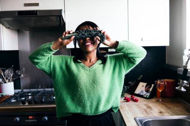 Smiling woman covering eyes with kale in kitchen at home model released Symbolfoto property released ASGF01609