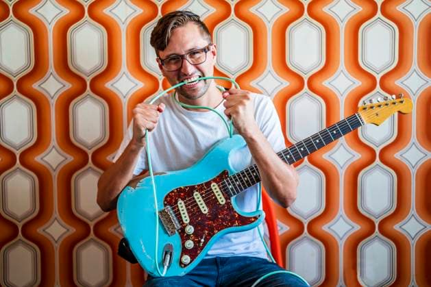 Young male guitarist biting guitar cable in front of wall model released Symbolfoto property released DLTSF02242