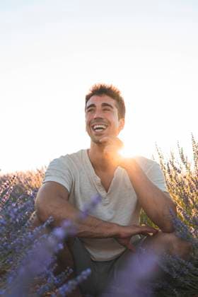 Cheerful man with hand on chin at lavender field model released Symbolfoto JAQF00812