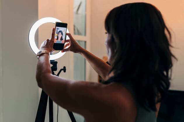 IMAGO Creative: Clickbait, Sport und Fitness Mature female influencer adjusting smart phone on ring light at home model released Symbolfoto property released JRVF01875