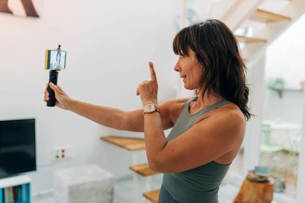 IMAGO Creative, Mainstream-Aktivismus Mature female influencer gesturing while filming video through smart phone at home model released Symbolfoto property released JRVF01877