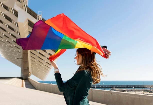 Woman holding rainbow flag near solar energy panel during sunny day model released Symbolfoto VABF04362