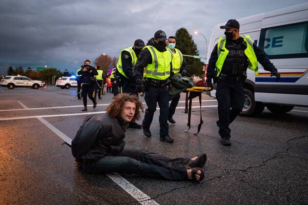 October 25, 2021, Richmond, BC, Canada: A handcuffed person sits on the ground after being taken into custody as RCMP officers use a stretcher to remove another protester after the environmental activist group Extinction Rebellion blocked the main road used to access Vancouver International Airport, in Richmond, B.C., Monday, Oct. 25, 2021. More than a dozen people were arrested and traffic to and from the airport was diverted due to the protest which was part of the group s two week October Rebellion action. Richmond Canada  - ZUMAc35_ 20211025_zaf_c35_139 Copyright: xDarrylxDyckx