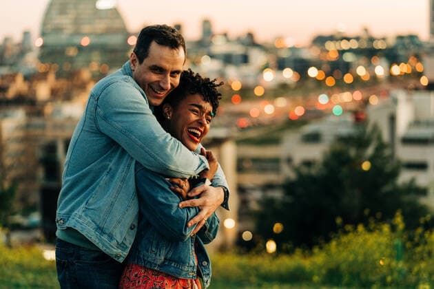 IMAGO Creative: Urban Diversity Romantic diverse couple embracing and looking away while standing on lawn against cityscape with buildings on blurred background, Model released JakeJakab_EliAndSergio_34.jpg Copyright: xJakexJakabx MR