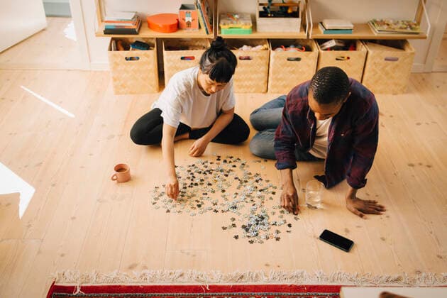 Multiracial male and female friend playing jigsaw puzzle at home Sweden, Stockholm, model released, property released Copyright: xMaskotx , MA90016