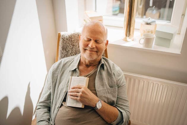Smiling senior man with book relaxing on chair at home Sweden, Stockholm, model released, property released Copyright: xMaskotx , MA90029