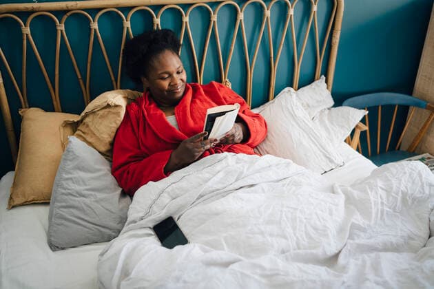 Smiling woman reading book on bed at home Sweden, Stockholm, model released, property released Copyright: xMaskotx , MA90066