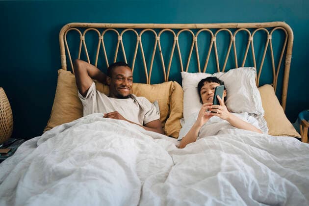 Smiling girlfriend sharing smart phone with boyfriend while lying on bed Sweden, Stockholm, model released, property released Copyright: xMaskotx , MA90084