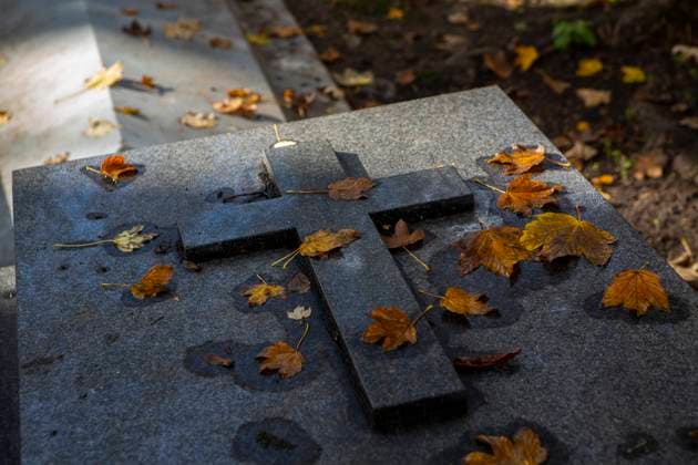 Ein Kreuz auf einem Grabstein, der von Herbstlaub bedeckt ist Symbolbild Trauer *** A cross on a gravestone covered by autumn leaves symbol image mourning