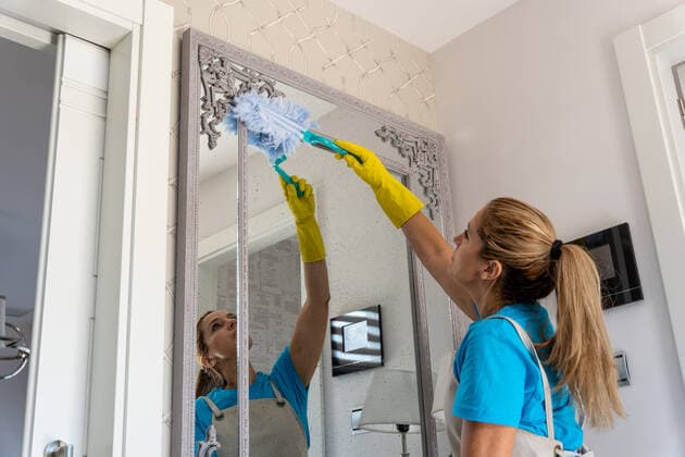 IMAGO Creative: Frühjahrsputz Side view of young female professional cleaner with long hair in uniform and gloves wiping mirror with dust brush during work in elegant apartment, Model released LuisBaneres_CleaningCrew_47.jpg Copyright: xLuisxBaneresx MR