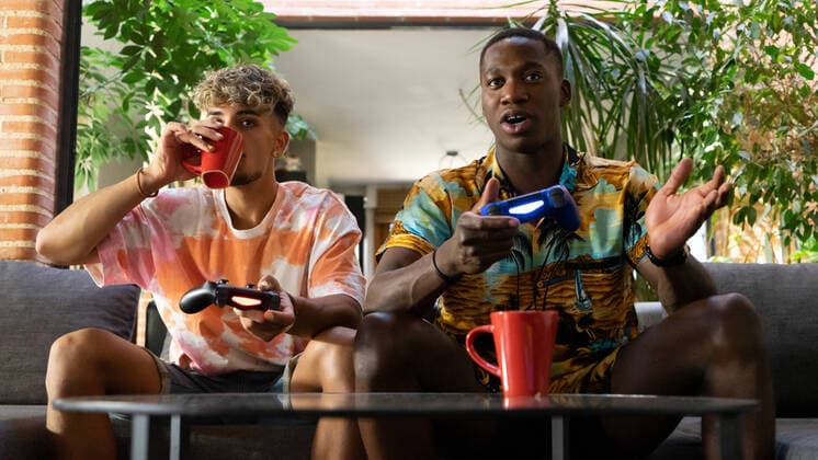 IMAGO Creative: Jahreszeit Winter, Couching Diverse male friends with gamepads drinking beverages while sitting on couch and playing video game together in living room with green plant, Model released SheyNunez_JeffreyAndRodrigo_15.jpg Copyright: xSheyxNunezx MR