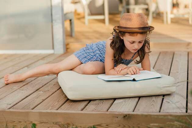  Mädchen sitzt auf Polster auf Holzterrasse und liest ein Buch *** Girl sitting on cushion on wooden terrace reading a book Copyright: imageBROKER/MichaelaxBegsteiger ibxbeg06967121.jpg