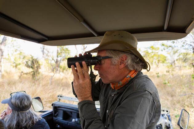 Safari guide using binoculars in a jeep with a family Okavango Delta,Botswana,Safari guide using binoculars in a jeep with a family  Safari guide using binoculars in a jeep with a family