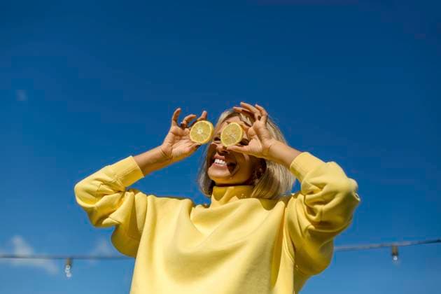 Cheerful woman holding slice of lemon in front of eyes during sunny day model released, LLUF00168