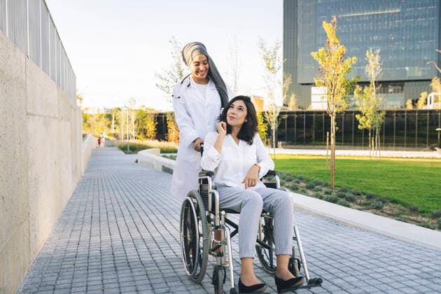 Disabled woman talking with female doctor pushing wheelchair on footpath model released, JCCMF04281