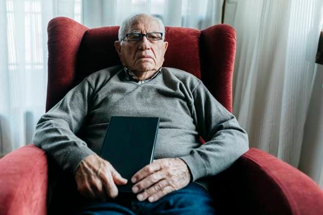 Senior man with book sitting on armchair model released property released, JRFF05191