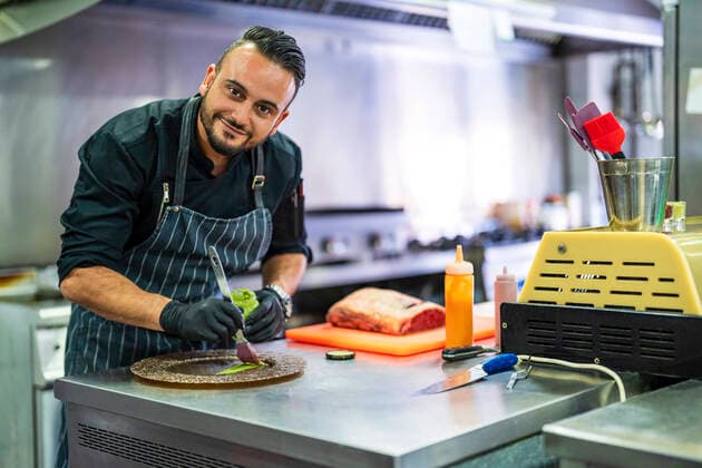 Smiling chef decorating plate for presentation in kitchen of restaurant model released property released, DLTSF02361