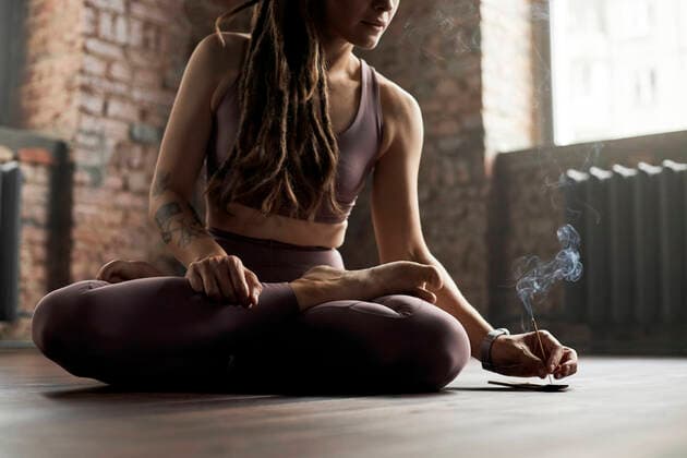 IMAGO Creative: Clickbait, Sport und Fitness Athlete sitting cross-legged holding burnt incense stick in yoga studio model released property released, DSHF00059
