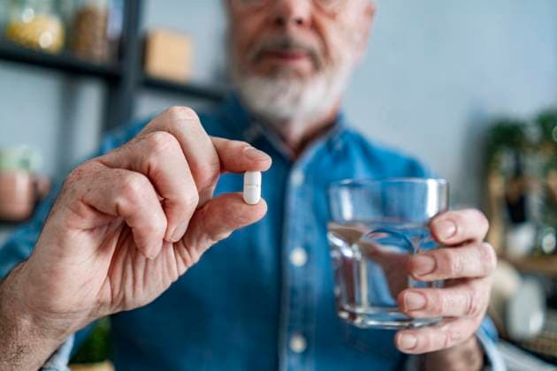 Senior man holding glass of water and pill at home model released property released, GIOF14152