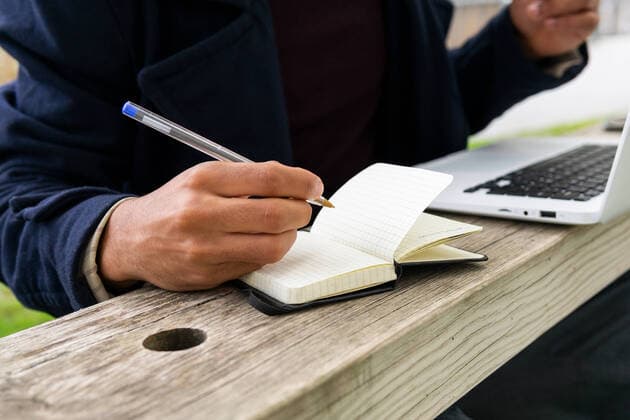 Cropped unrecognizable African American male student in outerwear sitting on bench and taking notes in notepad while doing homework on netbook in park, Model released DavidMunoz_MarceloAtForum_19.jpg Copyright: xDavidxMunozx MR