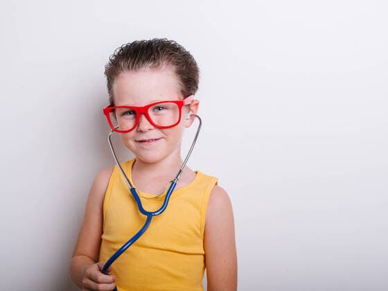 Positive girl in red eyeglasses with stethoscope while looking at camera and playing doctor on white background in light studio, Model released HodeiUnzueta_DisguisedKids_47.jpg Copyright: xHodeixUnzuetax MR