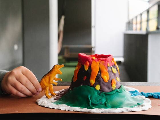 Crop anonymous kid playing with toy dinosaur and plasticine volcano figurine at wooden table on balcony, Model released HodeiUnzueta_Volcano_14.jpg Copyright: xHodeixUnzuetax MR