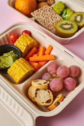 From above of lunch boxes with healthy food including crackers carrot sticks grapes cherry tomatoes with kiwi broccoli walnut and tangerine on pink background RamonLopez_Lunchboxes_24.jpg Copyright: xRamonxLopezx Model Released