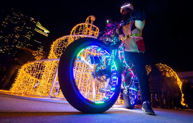 (211128) -- TORONTO, Nov. 28, 2021 -- A man riding a bicycle decorated with LED lights poses for photos in front of a light installation during the 2021 Cavalcade of Lights in Toronto, Canada, Nov. 27, 2021. The annual light show in Toronto kicked off on Saturday and will last until Jan. 2, 2022. (Photo by Xinhua) CANADA-TORONTO-LIGHT SHOW ZouxZheng 