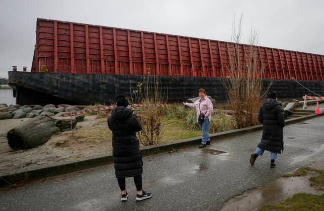(211129) -- VANCOUVER, Nov. 29, 2021 -- A woman poses for a photo with the barge washed up at Sunset Beach in Vancouver, Canada, Nov. 28, 2021. The barge was washed up on Sunset Beach two weeks ago due to the windstorm. (Photo by Xinhua) CANADA-VANCOUVER-BARGE-BEACH LiangxSen 