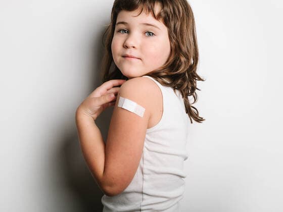Side view of schoolgirl after vaccination standing with band aid on arm and looking at camera, Model released HodeiUnzueta_VaccinatedKids_18.jpg Copyright: xHodeixUnzuetax MR