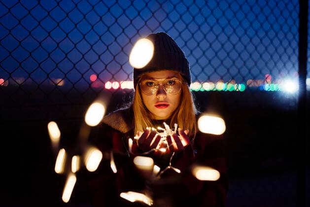 Creative Highlights Symbolbilder Pretty blonde young woman with wool hat and glasses holding a light garland of lights looking at the camera on the street, Model released ManuelRuizAlba_BlondieYoungWoman_41.jpg Copyright: xManuelxRuizxAlbax MR